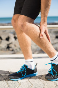 Fit man gripping his injured calf muscle on a sunny day